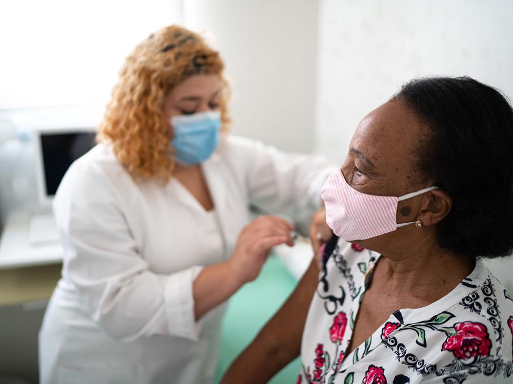 One masked woman provides another masked woman with a vaccine in her right arm.