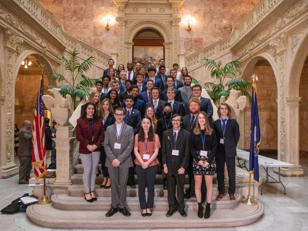 Penn State students standing on steps in an ornate room in the Pennsylvania state capitol building