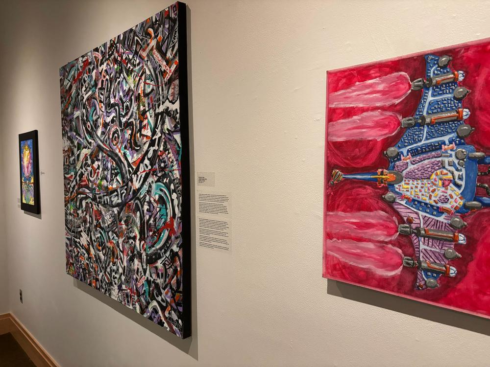 Art gallery wall with three colorful abstract paintings, including bold red, graffiti-style, and vibrant fantasy-themed works.